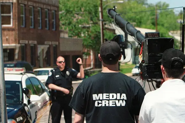 media crew filming a copy by his car on a street