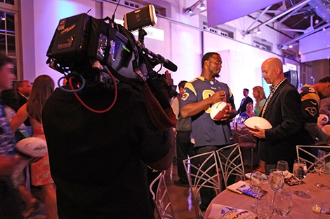 Video camera filming a Rams football players signing a football while talking to a person holding a football
