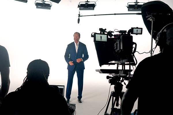 Man in a suit laughing on camera in a white background video studio setup