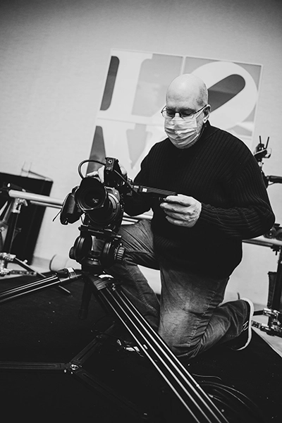 Man wearing a surgical mask kneeling on the ground aiming a camera